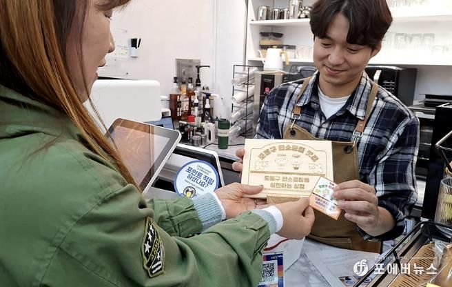 구 직원이 탄소중립 맛집 가게에 안내판을 전달하고 있다.